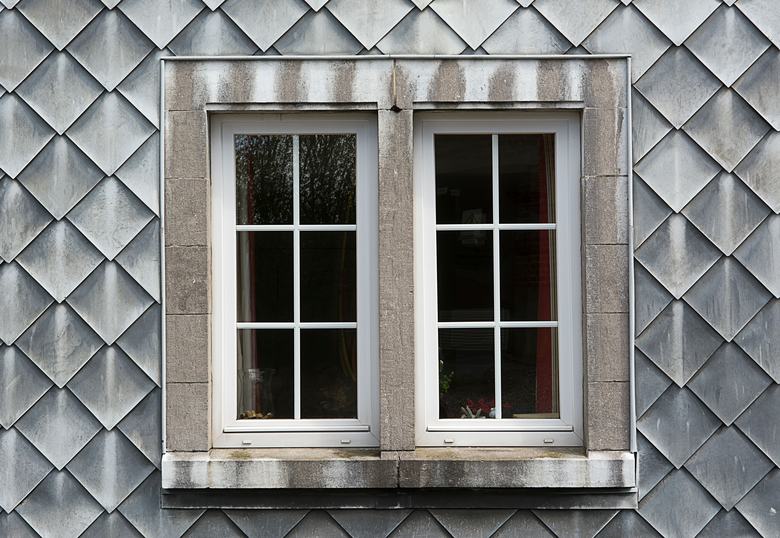 Double fenêtre blanche à petits carreaux sur une façade en ardoise